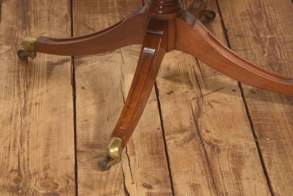 An oval mahogany coffee table featuring an inset green tooled leather border, a central turned pedestal stem, four swept legs, and brass castors. View V