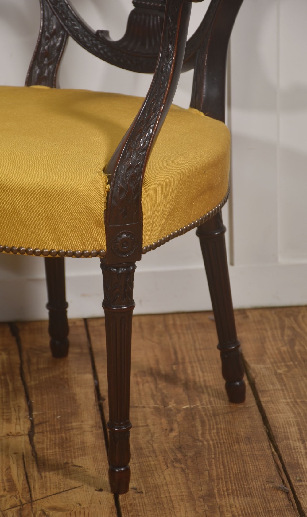 A carved mahogany open armchair featuring an oval wheat-sheaf backrest, swept arms, and a yellow upholstered seat secured with brass studs. View V