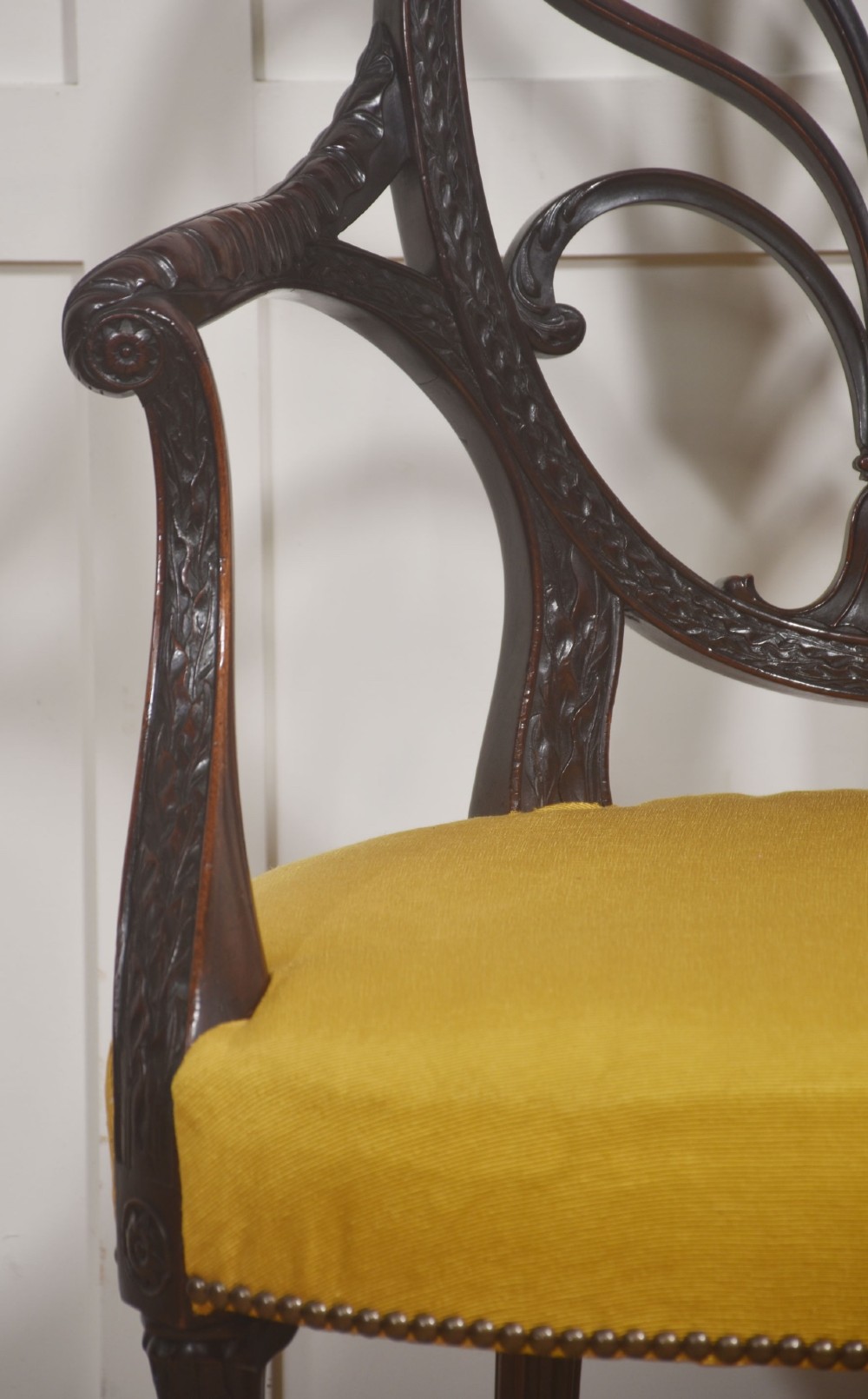 A carved mahogany open armchair featuring an oval wheat-sheaf backrest, swept arms, and a yellow upholstered seat secured with brass studs. View VI