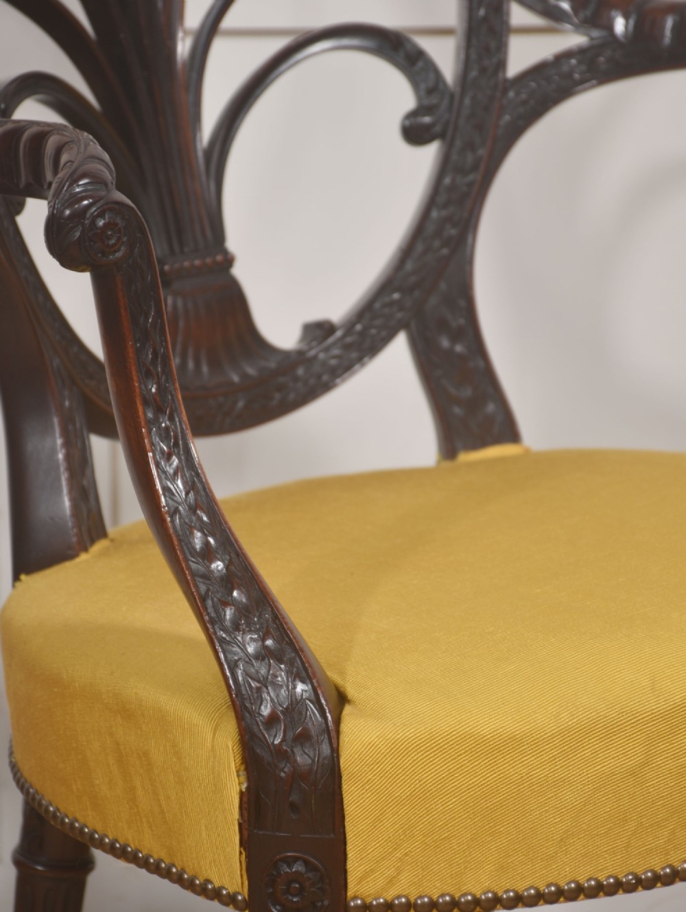 A carved mahogany open armchair featuring an oval wheat-sheaf backrest, swept arms, and a yellow upholstered seat secured with brass studs. View X