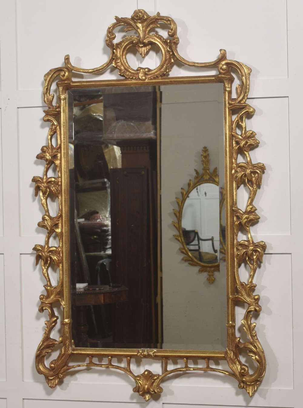 A rectangular wall mirror with a bevelled glass edge framed in elaborate carved gold giltwood featuring scrolls and acanthus motifs. View IX