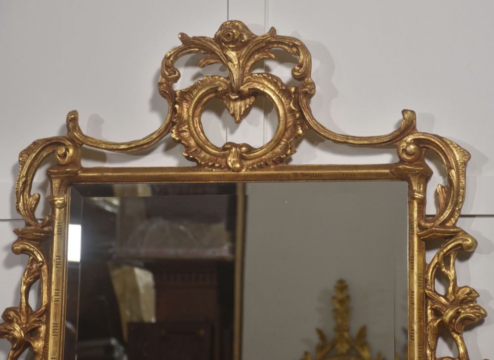 A rectangular wall mirror with a bevelled glass edge framed in elaborate carved gold giltwood featuring scrolls and acanthus motifs. View X