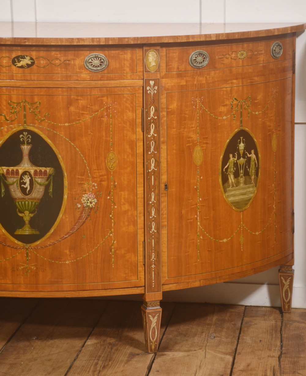 A pair of golden satinwood demi-lune cabinets featuring central hand-painted oval urn motifs and tapered legs. View IV