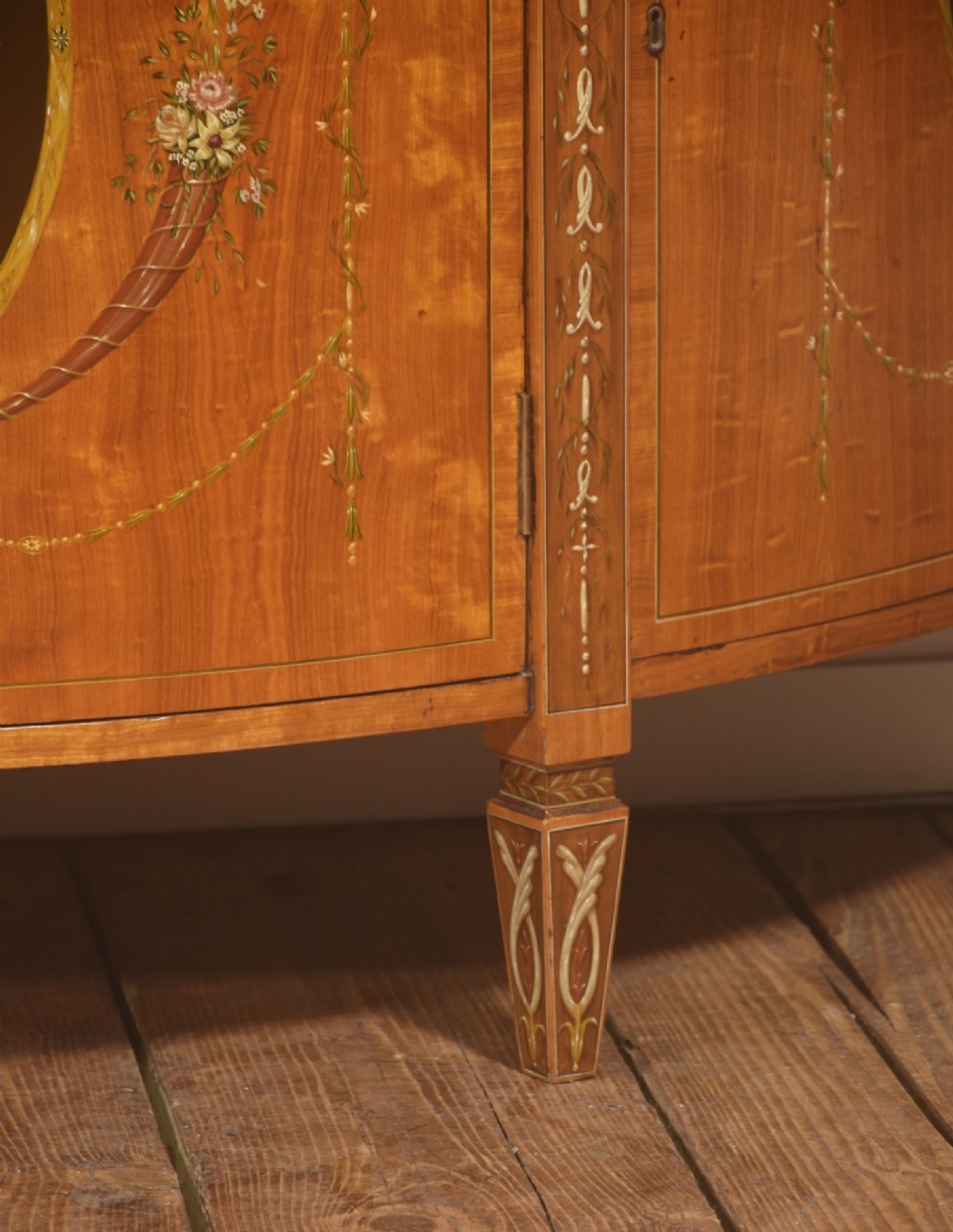 A pair of golden satinwood demi-lune cabinets featuring central hand-painted oval urn motifs and tapered legs. View IX