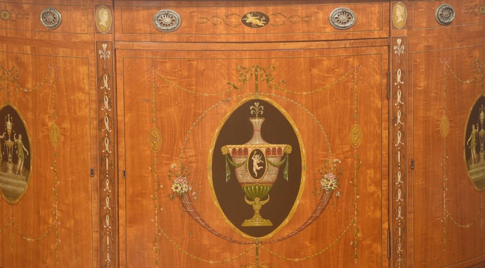A pair of golden satinwood demi-lune cabinets featuring central hand-painted oval urn motifs and tapered legs. View XI