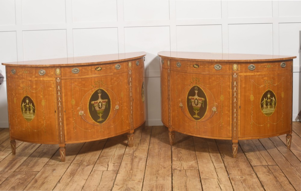 A pair of golden satinwood demi-lune cabinets featuring central hand-painted oval urn motifs and tapered legs. View XII