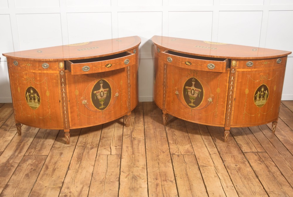 A pair of golden satinwood demi-lune cabinets featuring central hand-painted oval urn motifs and tapered legs. View XIII