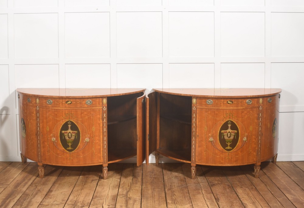 A pair of golden satinwood demi-lune cabinets featuring central hand-painted oval urn motifs and tapered legs. View XIV
