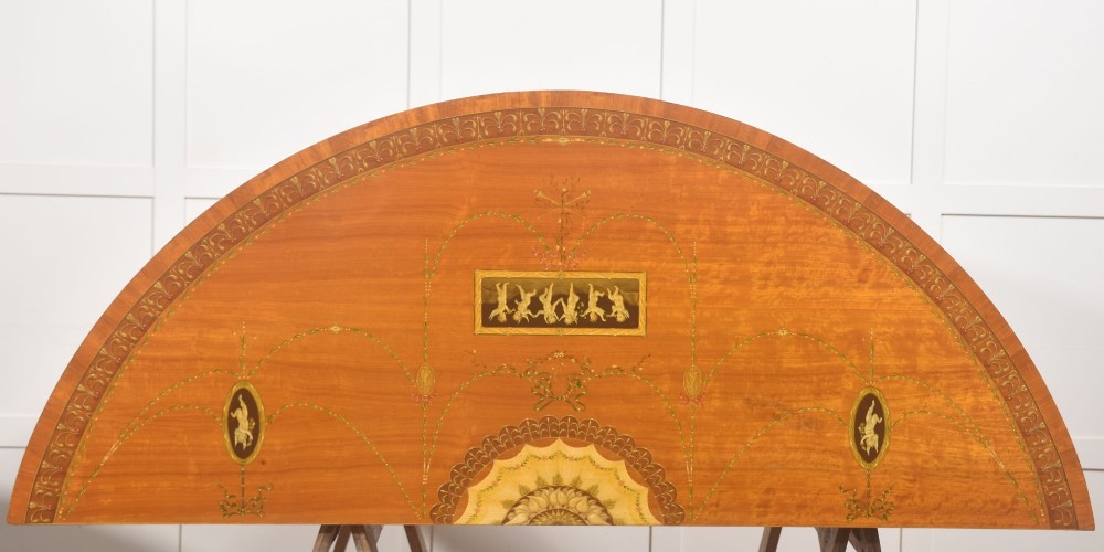 A pair of golden satinwood demi-lune cabinets featuring central hand-painted oval urn motifs and tapered legs. View XV