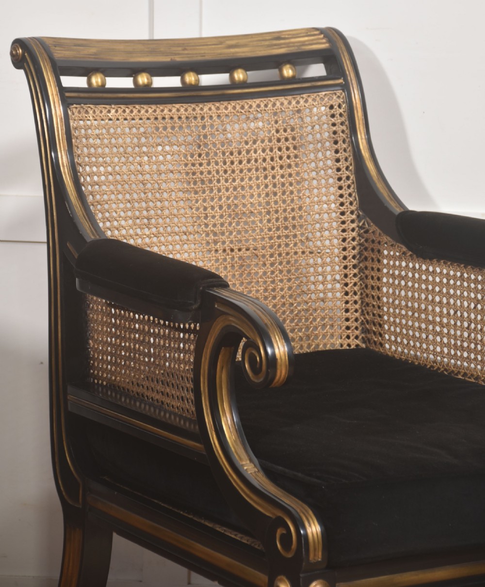 A pair of ebonised and parcel-gilt armchairs featuring woven cane backs, scroll arms, black upholstered cushions, and brass castors. View III