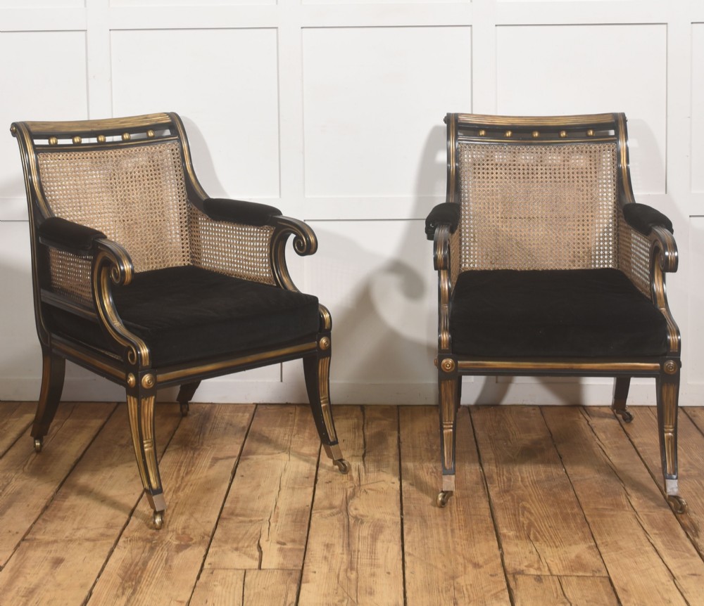 A pair of ebonised and parcel-gilt armchairs featuring woven cane backs, scroll arms, black upholstered cushions, and brass castors. View IX