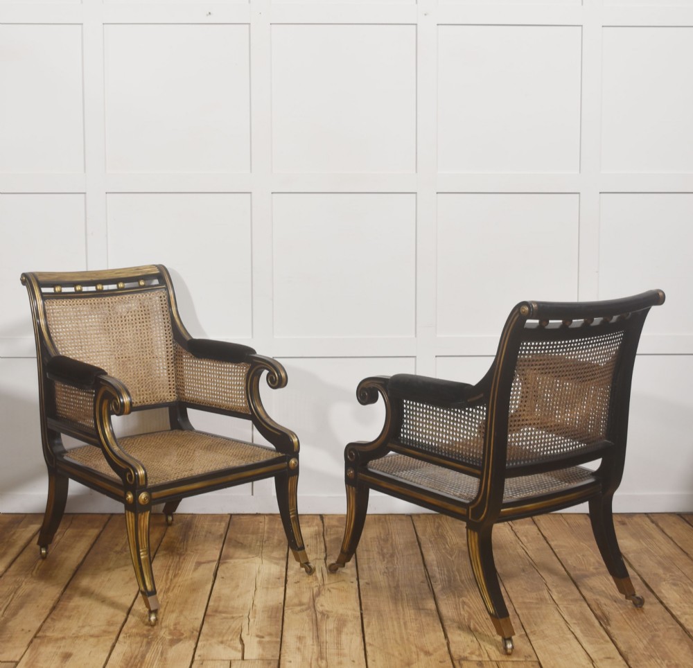 A pair of ebonised and parcel-gilt armchairs featuring woven cane backs, scroll arms, black upholstered cushions, and brass castors. View XI