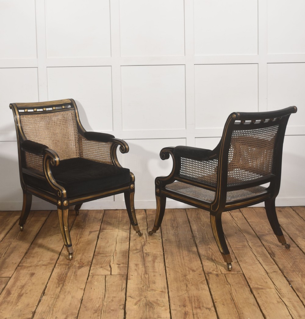 A pair of ebonised and parcel-gilt armchairs featuring woven cane backs, scroll arms, black upholstered cushions, and brass castors. View XII