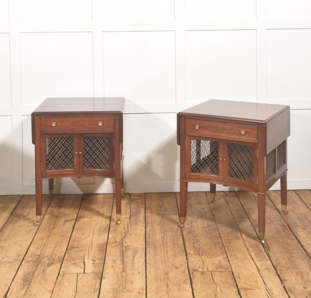 A pair of rosewood drop-leaf side tables featuring single drawers above cupboard doors with brass grille inserts, standing on square tapered legs with brass castors.
