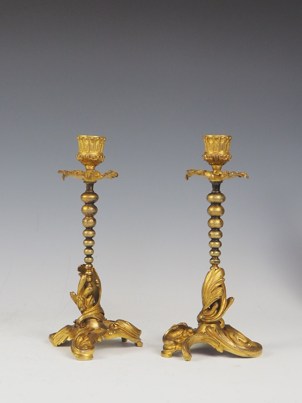 A pair of nineteenth-century French gilt bronze candlesticks featuring acanthus leaf scroll bases, beaded stems, and fluted sconces.