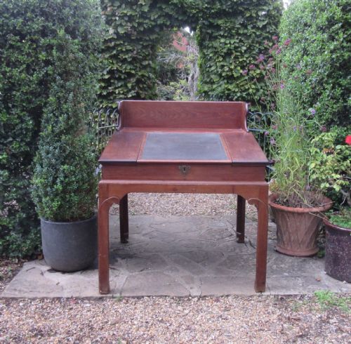 fig 1. A Georgian mahogany estate desk featuring a slanted writing surface with a dark inset leather skiver, raised scrolled gallery back, and square legs with decorative corner spandrels.