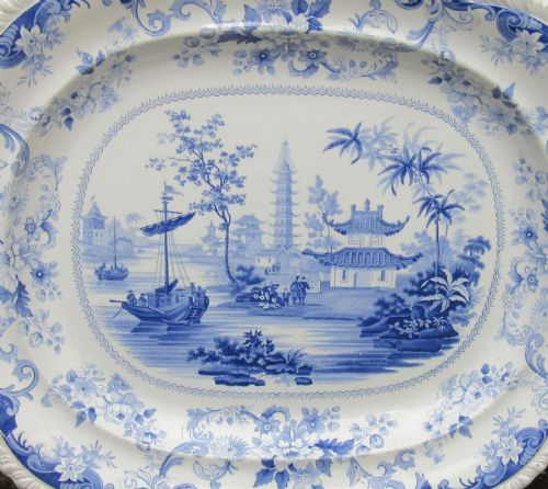fig 1. An oval earthenware platter featuring a blue and white printed Chinoiserie scene, surrounded by a floral scroll border with a moulded rim.