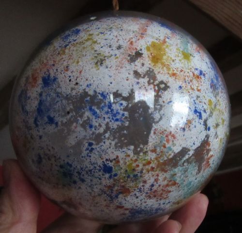 fig 1. A spherical Victorian potichomania glass witch ball featuring a white base with multicoloured speckled patterns of orange, blue, and yellow.