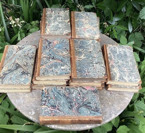 fig 1. An eighteen-volume collection of Georgian leather-bound books featuring gilt-tooled lettering and red spine labels.