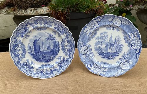fig 1. A group of six early 19th-century Staffordshire blue and white transferware ceramic plates displaying pastoral, coastal, and floral patterns with scalloped borders.