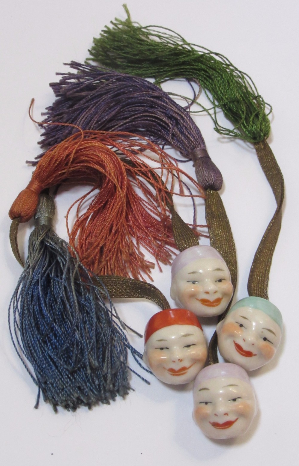FOUR CONTINENTAL PORCELAIN ORIENTAL FACES ON SILK TASSELS c1910