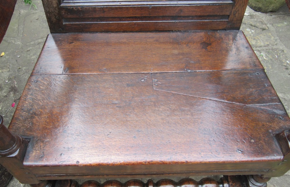 A seventeenth-century dark oak wainscot armchair featuring a carved cresting rail, panelled back, shaped arms, and a bobbin-turned front stretcher. View VII
