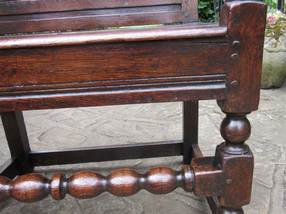 A seventeenth-century dark oak wainscot armchair featuring a carved cresting rail, panelled back, shaped arms, and a bobbin-turned front stretcher. View VIII