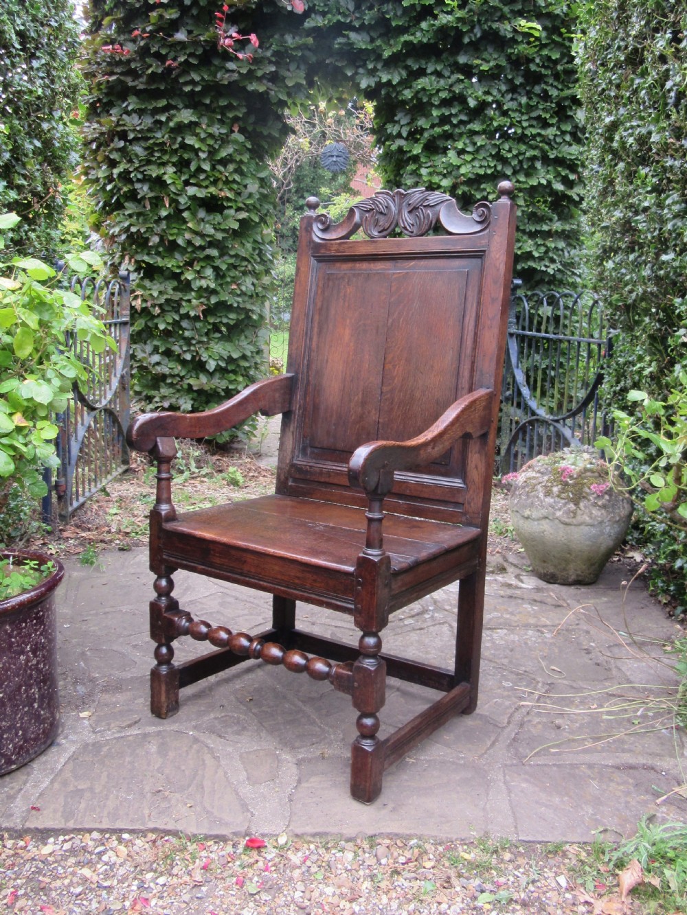 A seventeenth-century dark oak wainscot armchair featuring a carved cresting rail, panelled back, shaped arms, and a bobbin-turned front stretcher. View X