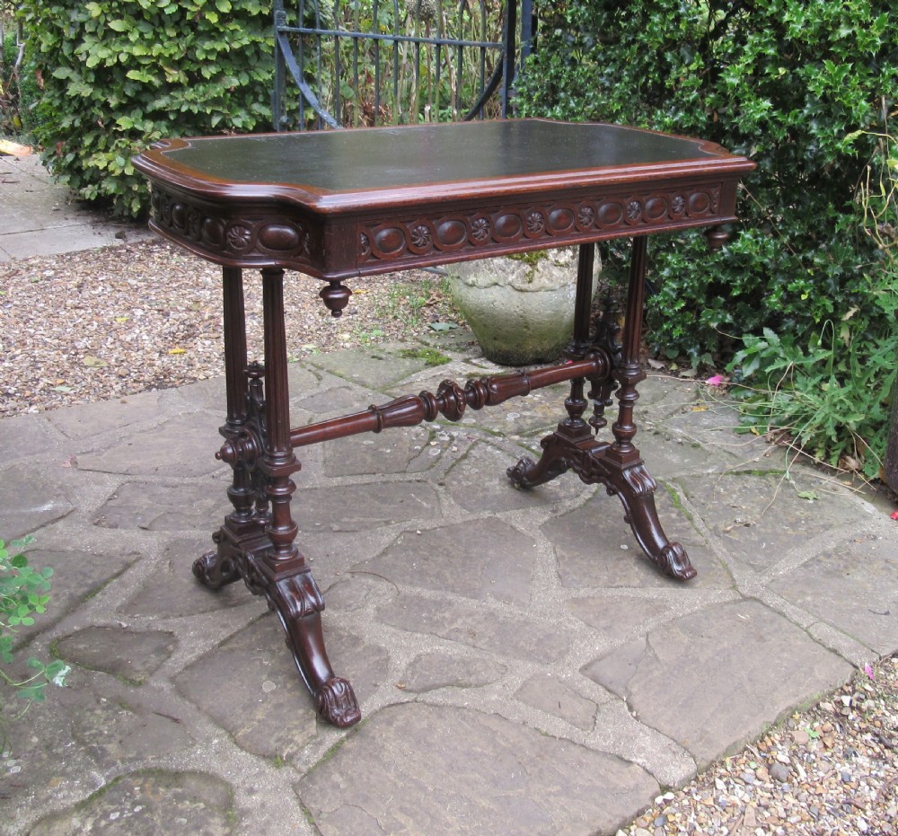 A mid-Victorian dark oak writing table featuring an inset green leather top, relief-carved aprons, turned trestle legs, and a central stretcher. View II