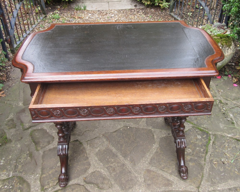 A mid-Victorian dark oak writing table featuring an inset green leather top, relief-carved aprons, turned trestle legs, and a central stretcher. View IV