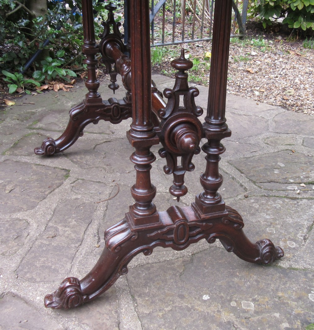 A mid-Victorian dark oak writing table featuring an inset green leather top, relief-carved aprons, turned trestle legs, and a central stretcher. View VI
