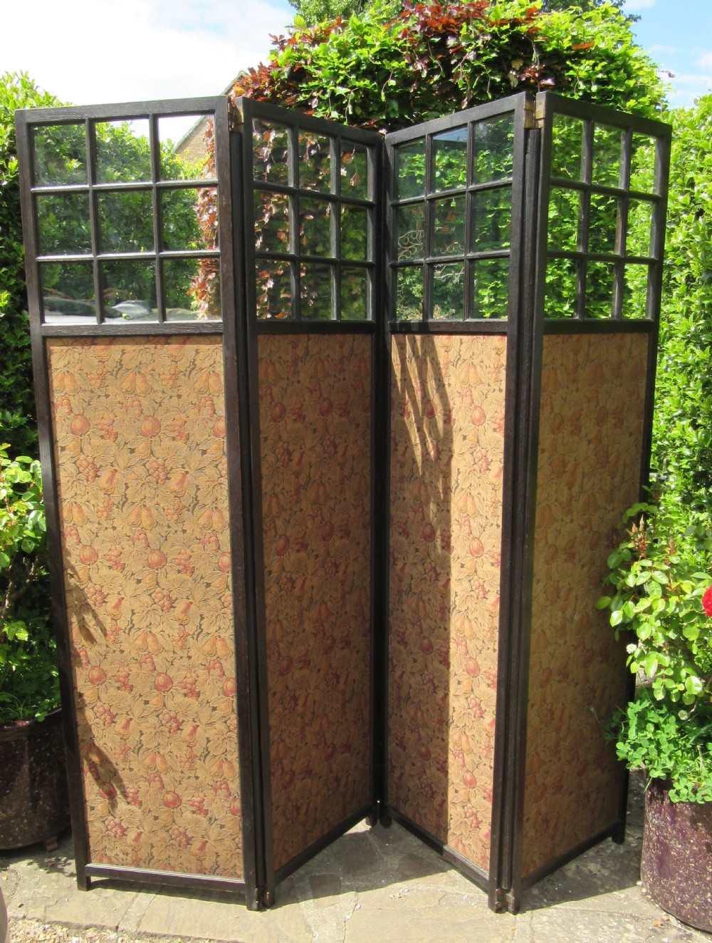 An Arts and Crafts four-panel ebonised oak folding screen featuring six glazed panes at the top of each panel and patterned botanical fabric inserts below. View II