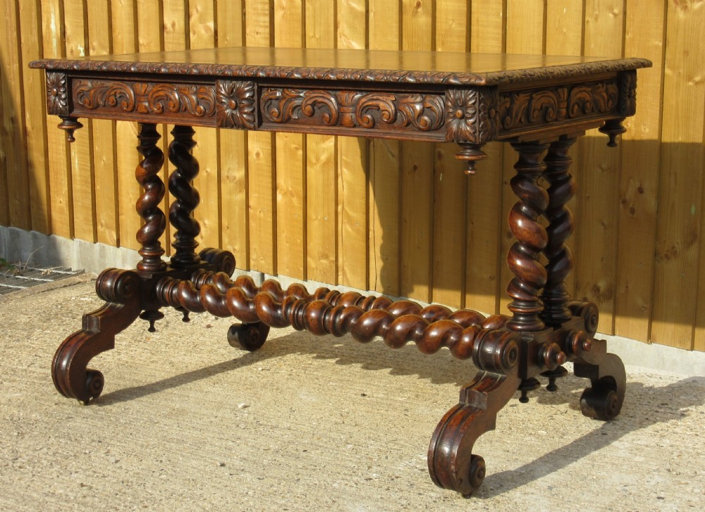 A late 19th-century dark oak writing table featuring relief-carved drawer fronts, barley twist legs, and a double twisted stretcher.