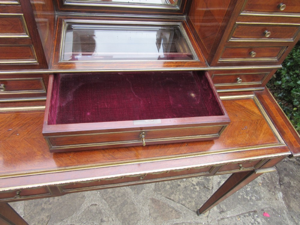 A late 19th-century rosewood bonheur du jour writing desk featuring brass gallery railings, an arched central mirror, multiple small drawers, and tapered legs. View V