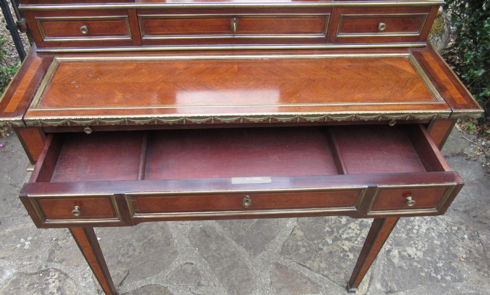 A late 19th-century rosewood bonheur du jour writing desk featuring brass gallery railings, an arched central mirror, multiple small drawers, and tapered legs. View VI