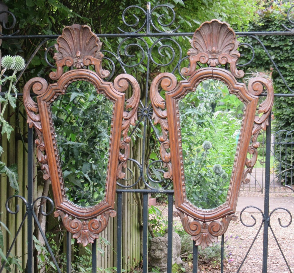A pair of early 20th-century carved pine wall mirrors featuring shell crests and intricate scrollwork frames.