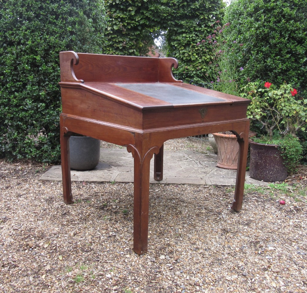 A Georgian mahogany estate desk featuring a slanted writing surface with a dark inset leather skiver, raised scrolled gallery back, and square legs with decorative corner spandrels.