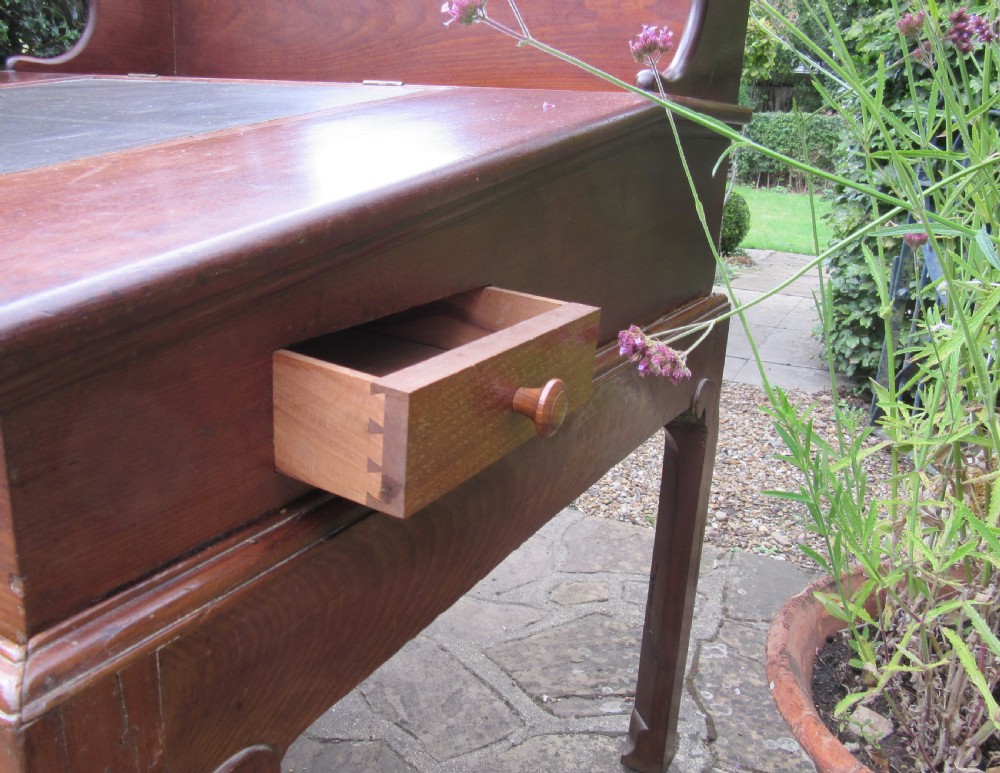 A Georgian mahogany estate desk featuring a slanted writing surface with a dark inset leather skiver, raised scrolled gallery back, and square legs with decorative corner spandrels. View V