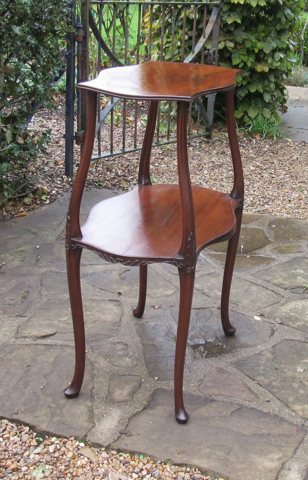 An Edwardian mahogany lamp table featuring a serpentine-shaped top, lower shelf, and four slender cabriole legs with carved detail.