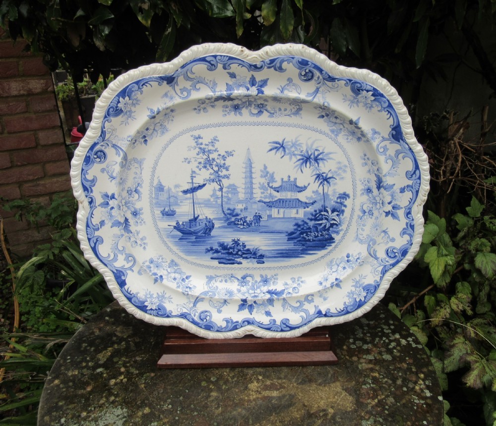 An oval earthenware platter featuring a blue and white printed Chinoiserie scene, surrounded by a floral scroll border with a moulded rim.