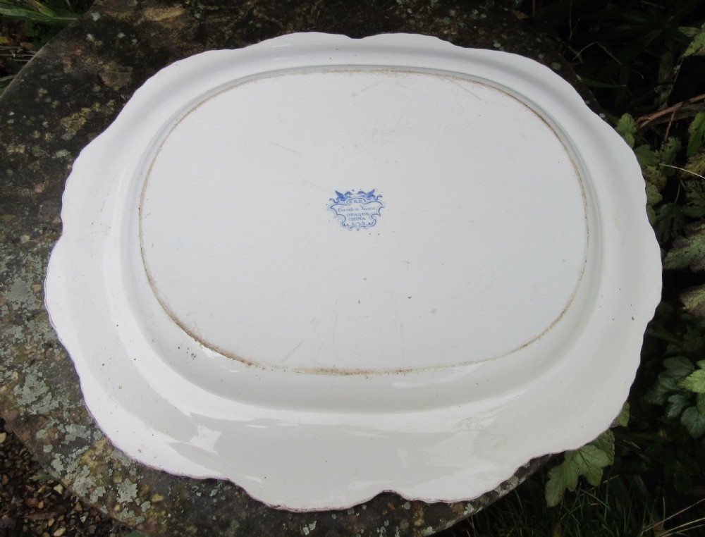 An oval earthenware platter featuring a blue and white printed Chinoiserie scene, surrounded by a floral scroll border with a moulded rim. View IV
