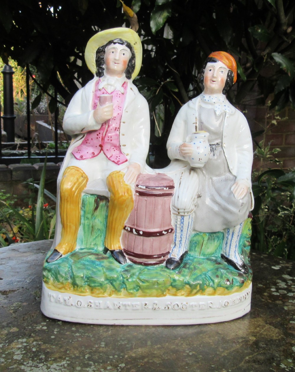 A Victorian lead-glazed earthenware figure group depicting two seated men, Tam o Shanter and Souter Johnny, painted in polychrome enamel colours on a moulded base.