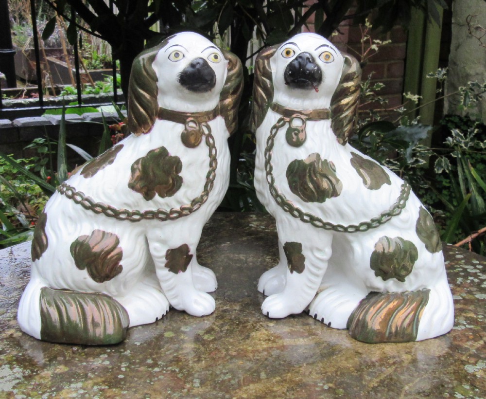 A pair of Victorian ceramic Staffordshire spaniel figurines featuring white glazed bodies with painted faces and copper lustre spots, ears, and moulded chains.