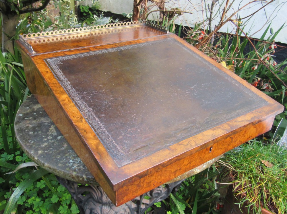 An antique Victorian figured walnut writing slope featuring a brass gallery rail and a brown leather writing surface with decorative gold tooling.