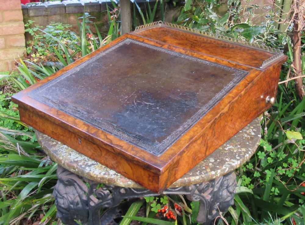 An antique Victorian figured walnut writing slope featuring a brass gallery rail and a brown leather writing surface with decorative gold tooling. View II