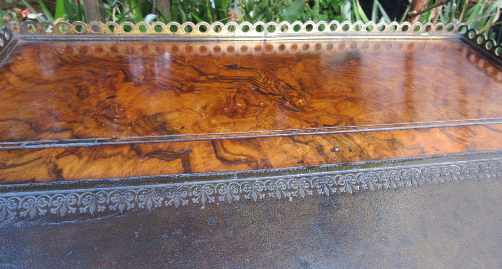 An antique Victorian figured walnut writing slope featuring a brass gallery rail and a brown leather writing surface with decorative gold tooling. View VII
