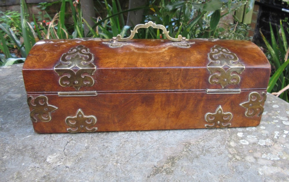A mid-19th-century domed-top box crafted from warm brown burr walnut wood, featuring ornate pierced brass strapwork mounts, a top handle, and a key inserted into the front lock. View II