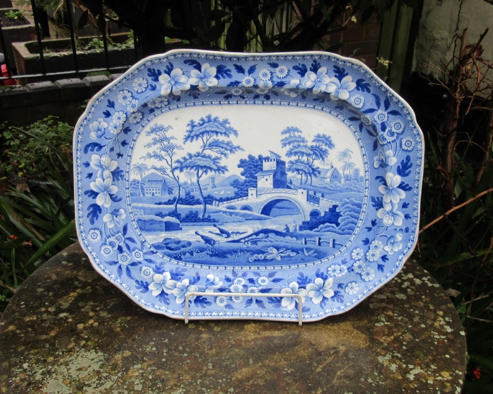 An oval blue and white earthenware serving platter with a central bridge landscape scene and a floral border.