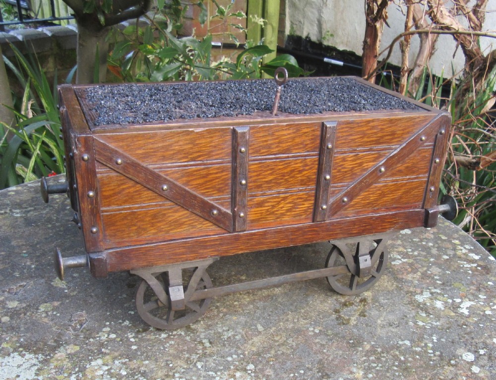 A late Victorian oak humidor designed in the form of a miniature railway coal wagon with metal wheels, buffers, and brass studs.