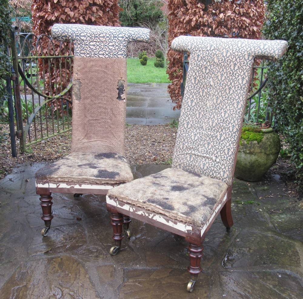 A pair of early Victorian rosewood prie-dieu chairs featuring tall T-bar backs, turned front legs on brass castors, and worn patterned upholstery.